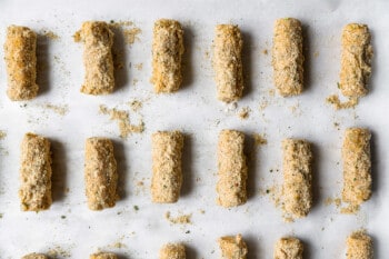 breaded mozzarella sticks lined up on parchment paper.