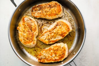 4 seared chicken breasts in a stainless pan.