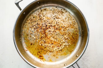 garlic and red pepper flakes cooking in oil in a stainless pan.