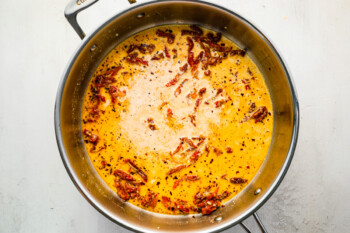 chicken broth, heavy cream, and sun-dried tomatoes added to garlic, red pepper flakes, and oil in a stainless pan.