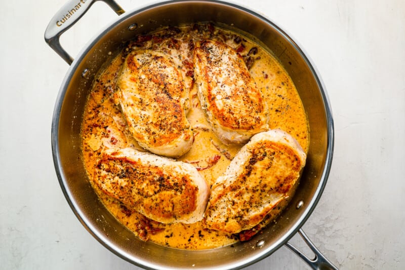 cooked chicken breasts nestled in sun-dried tomato cream sauce in a stainless pan.