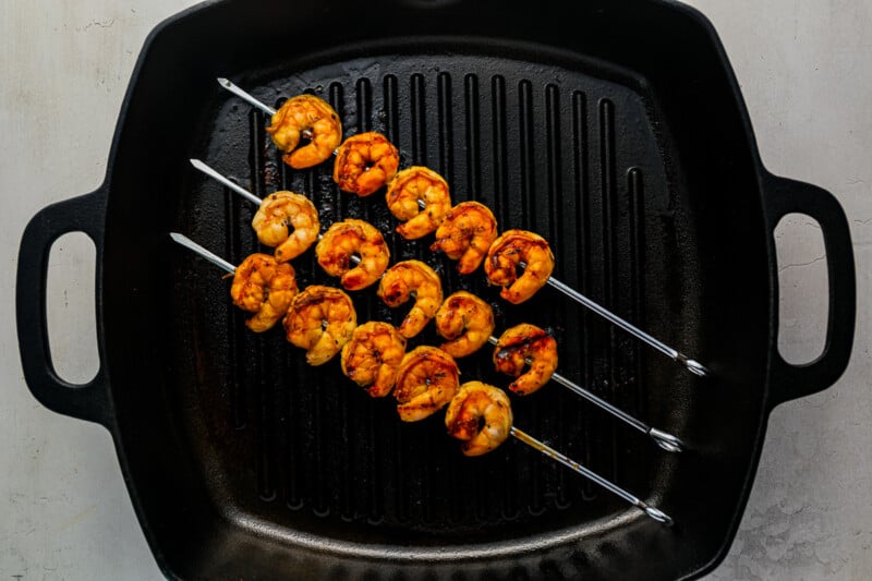 3 marinated shrimp on skewers in a grill pan.