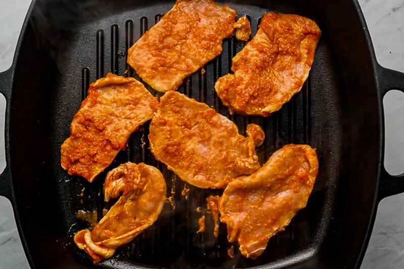 marinated pork in a skillet on a marble countertop.
