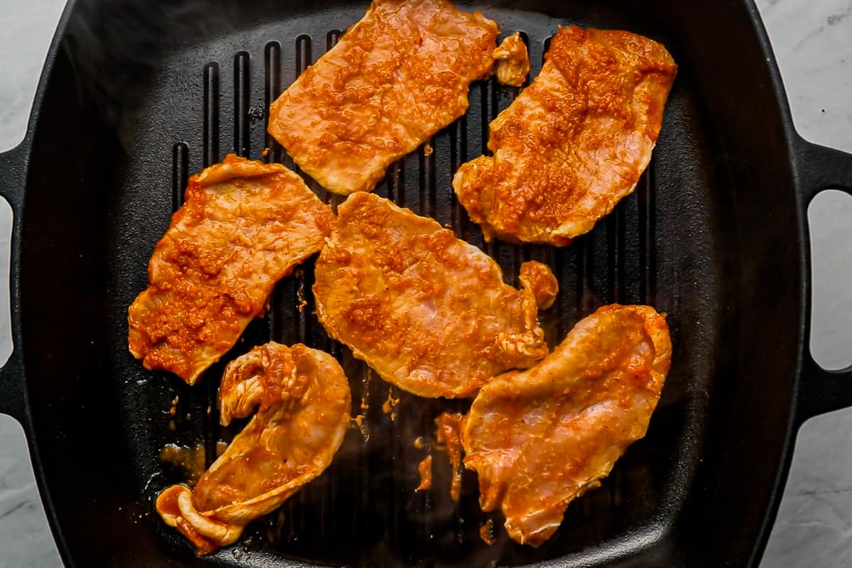 thin slices of pork cooking in a grill pan.