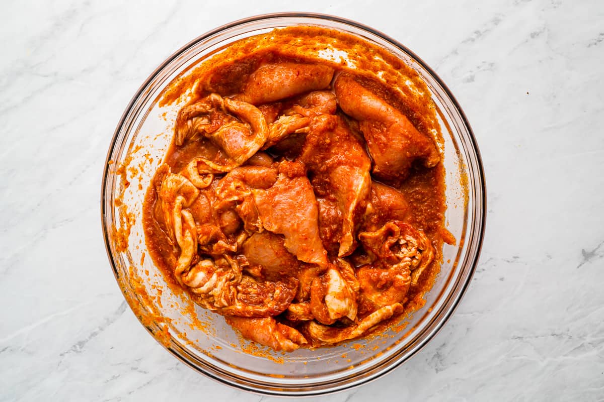 a glass bowl filled with pork marinating in a red sauce.
