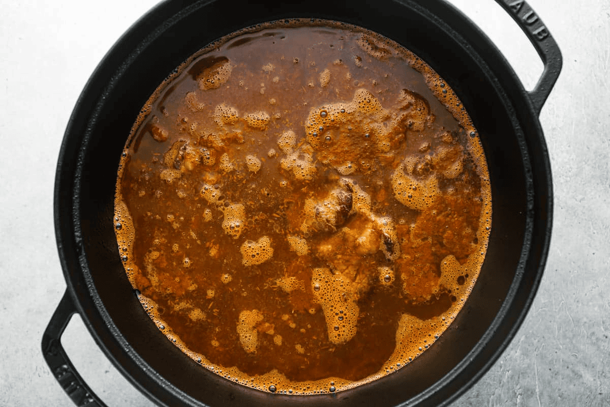 Cooking the quesabirria meat in the sauce and broth in a black pot. 