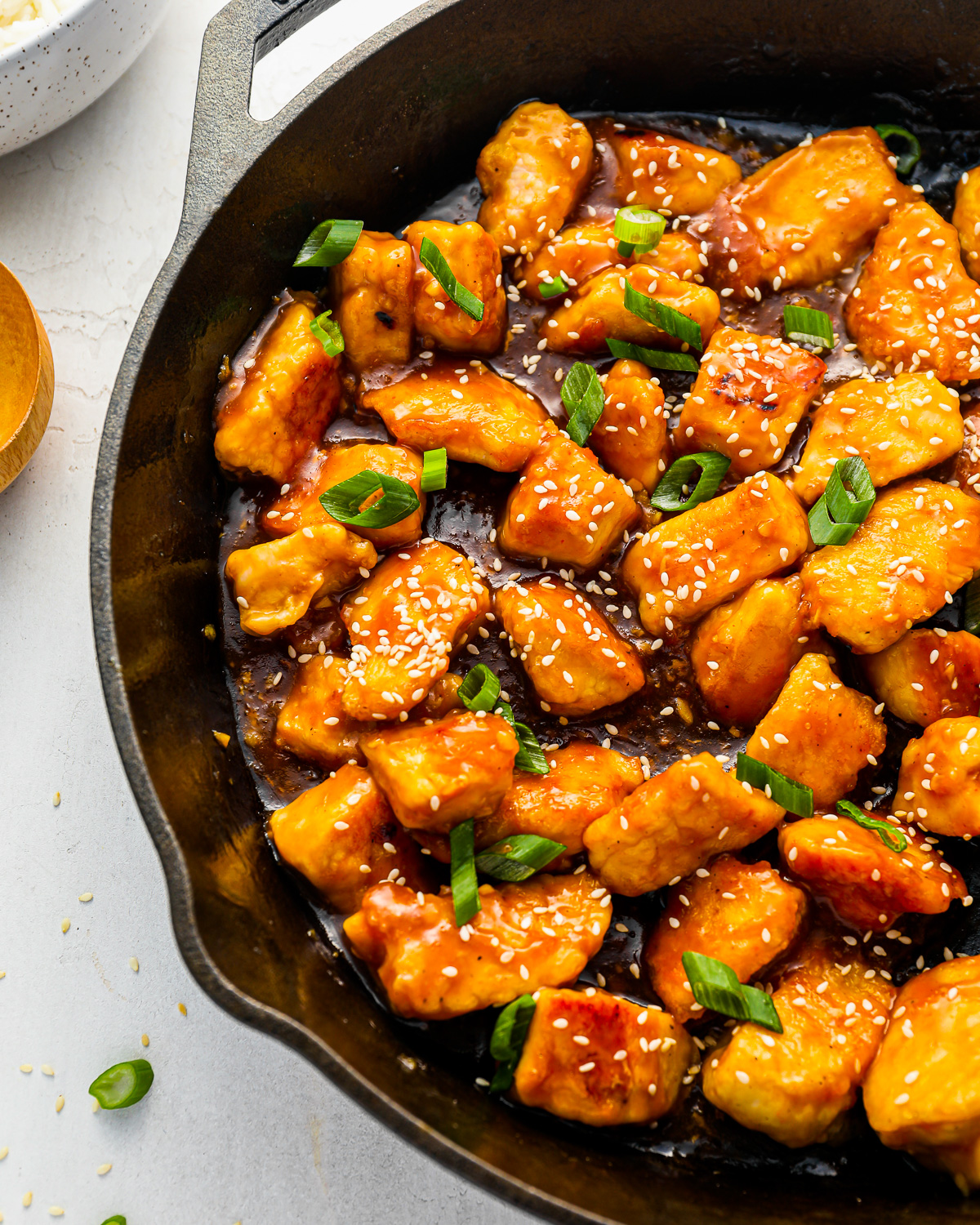 bites of chicken breast cooking in an orange sauce with sesame seeds, in a skillet.