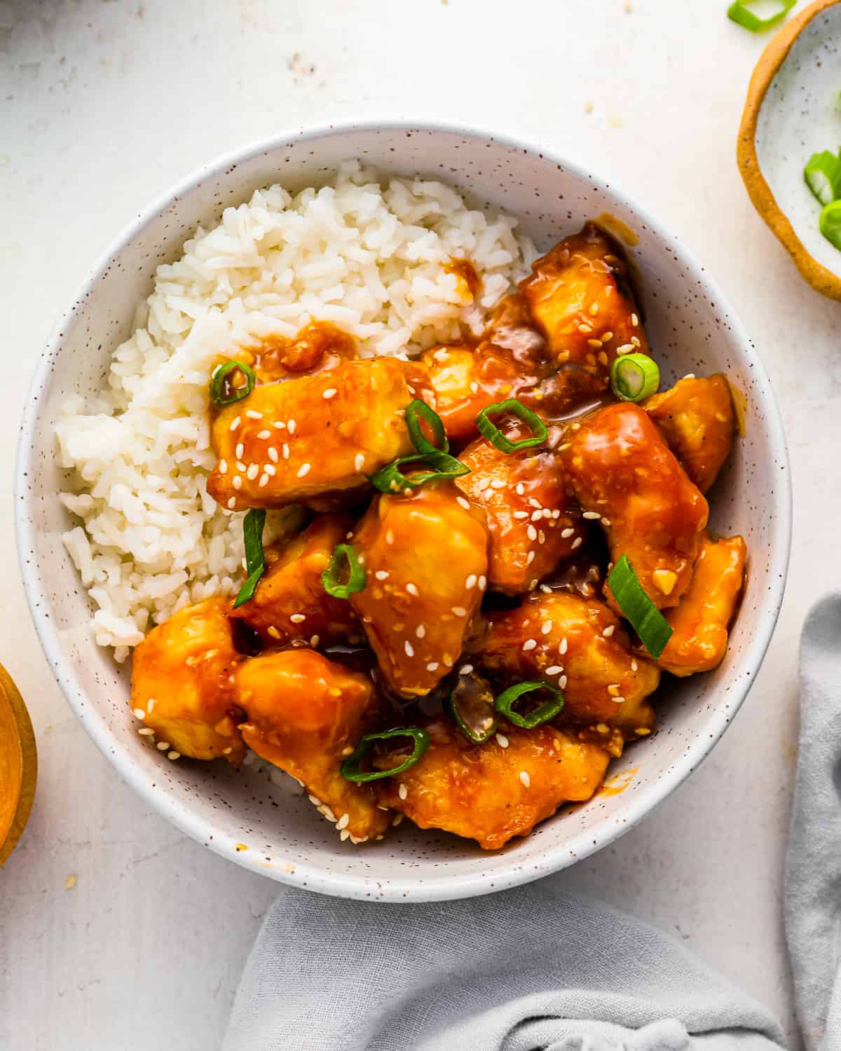 a bowl of orange chicken with white rice and sesame seeds.