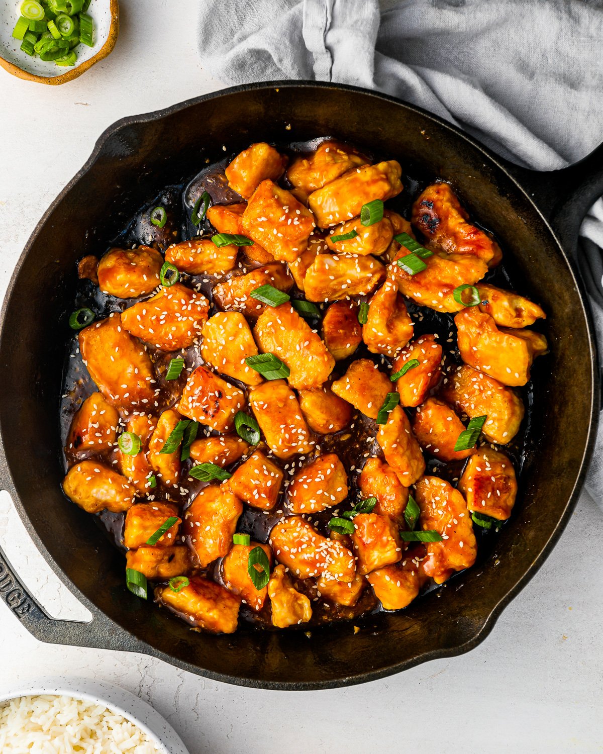 orange chicken in a skillet, sprinkled with sesame seeds and green onions.
