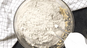A bowl of flour with a mixer in it, preparing for peanut butter blossoms.
