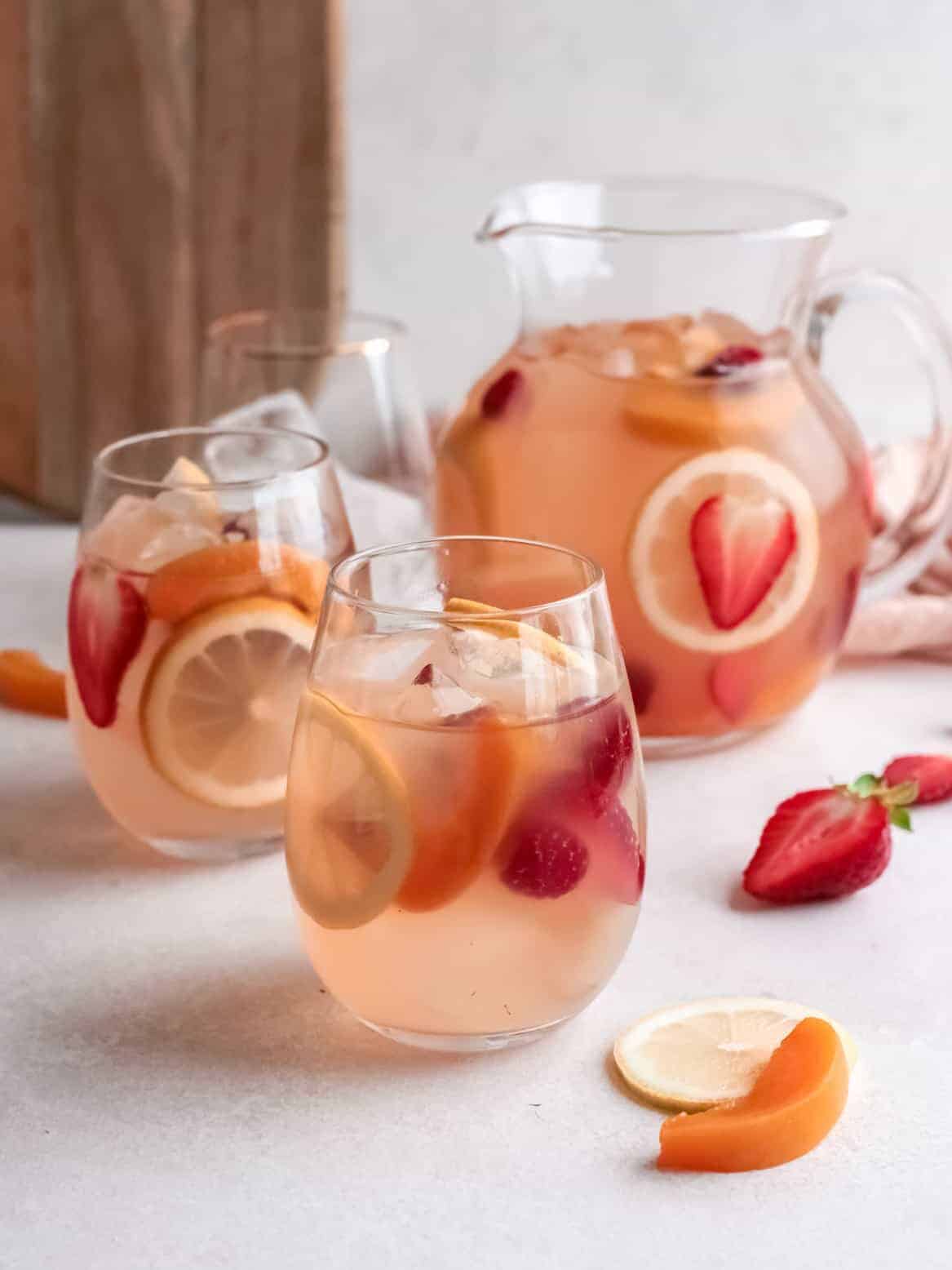 three-quarters view of 2 glasses of rose sangria in front of a pitcher.