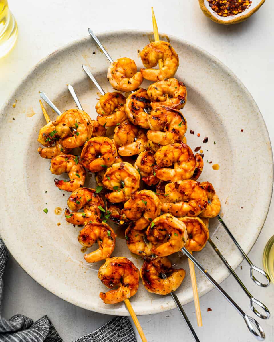 overhead view of 6 grilled shrimp skewers on a white plate.