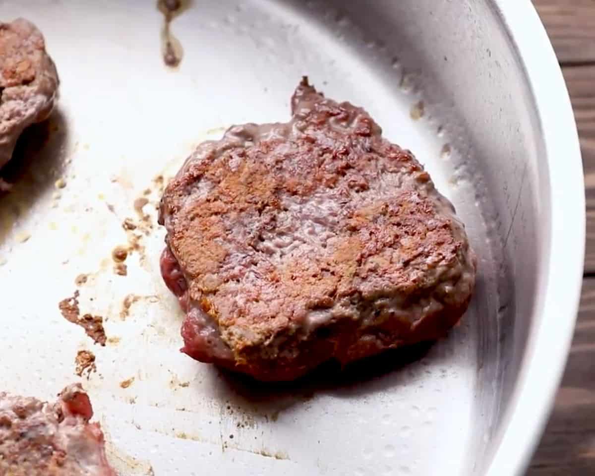 seared burger patty with a deeply browned crust, cooking in a skillet