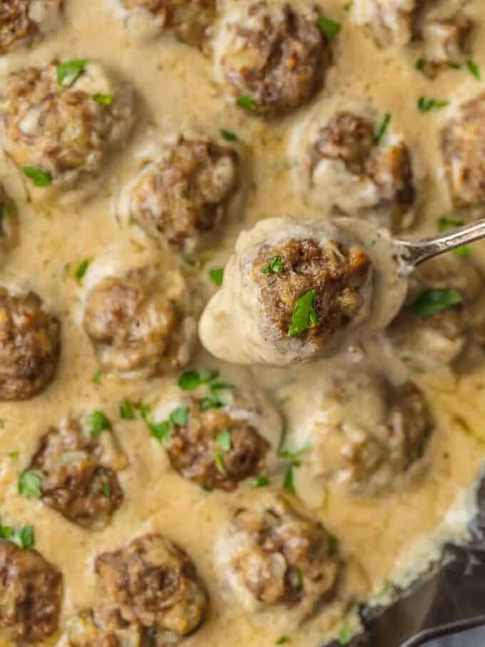 spoon holding up a meatball above a pan of meatballs in Swedish meatball gravy