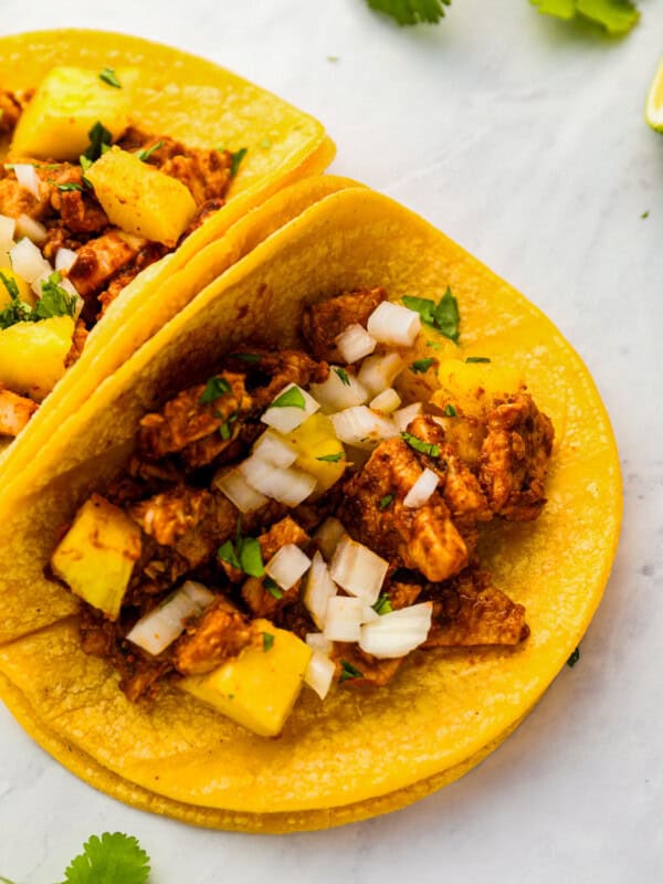 two tacos with chicken and pineapple on a white background.