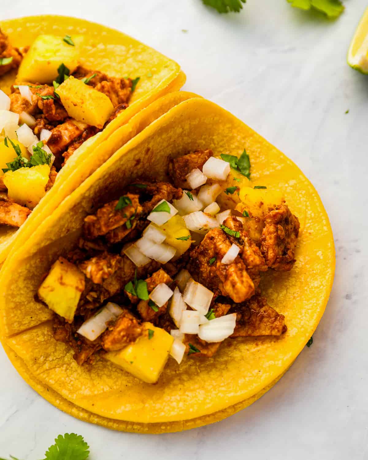 two tacos al pastor with pork and pineapple, on a white background.
