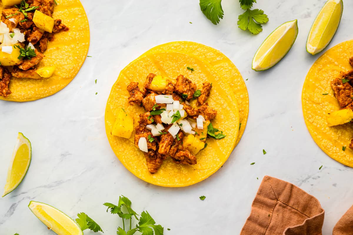 three tacos topped with grilled pork and pineapple.
