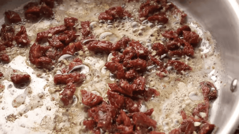 Tuscan chicken being cooked in a pan full of dried tomatoes soaked in oil.