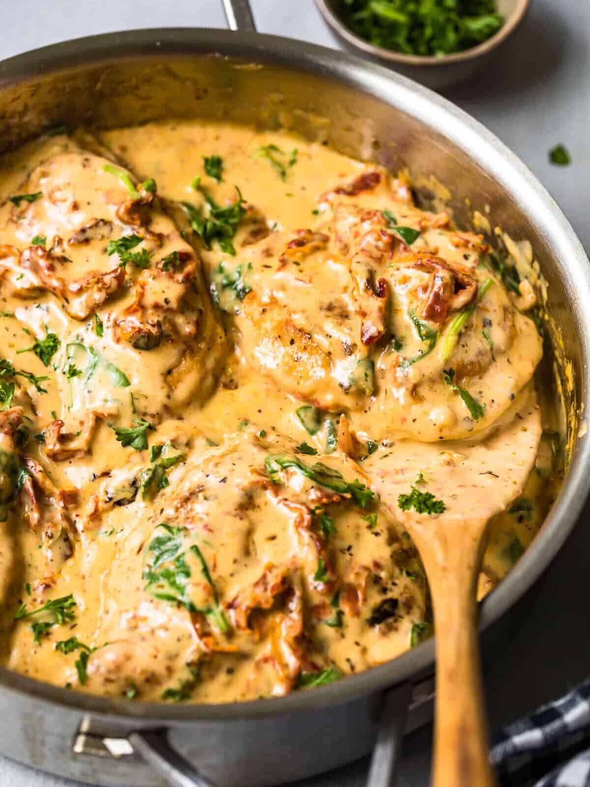 side shot of tuscan chicken in cream sauce with wooden spoon