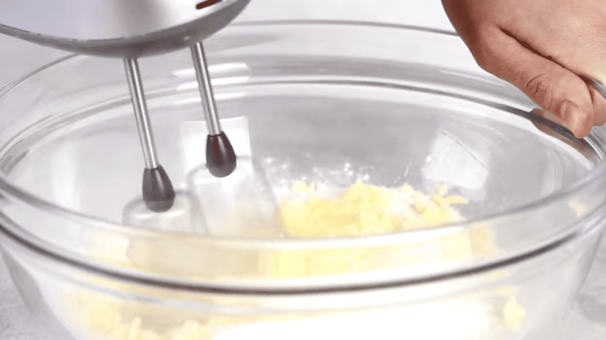 a hand mixer beating butter and sugar in a glass bowl.