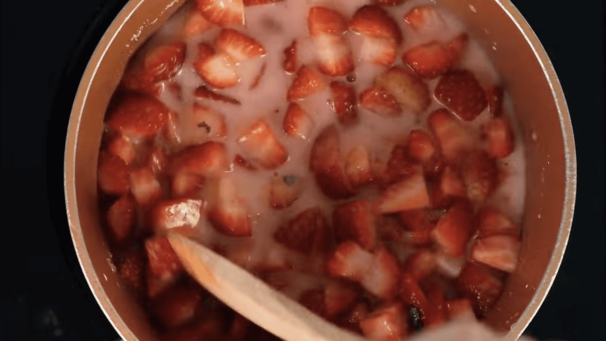 strawberries in white liquid in a saucepan with a wooden spoon.