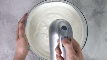 a hand mixer beating whipped cream in a glass bowl.