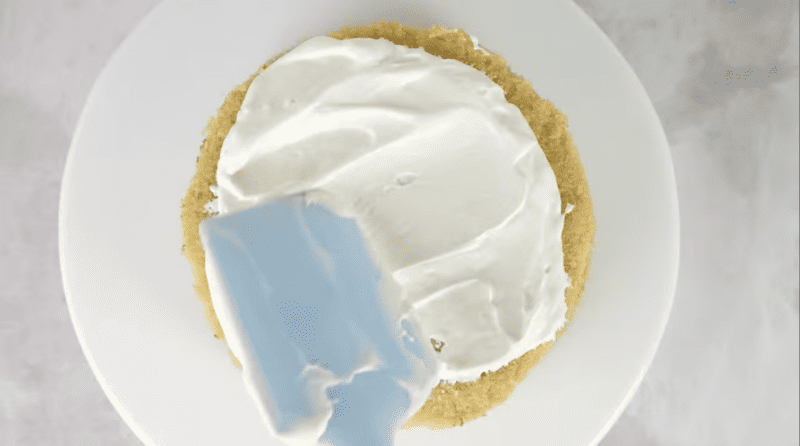 frosting spread over a cake round on a cake stand with a rubber spatula.