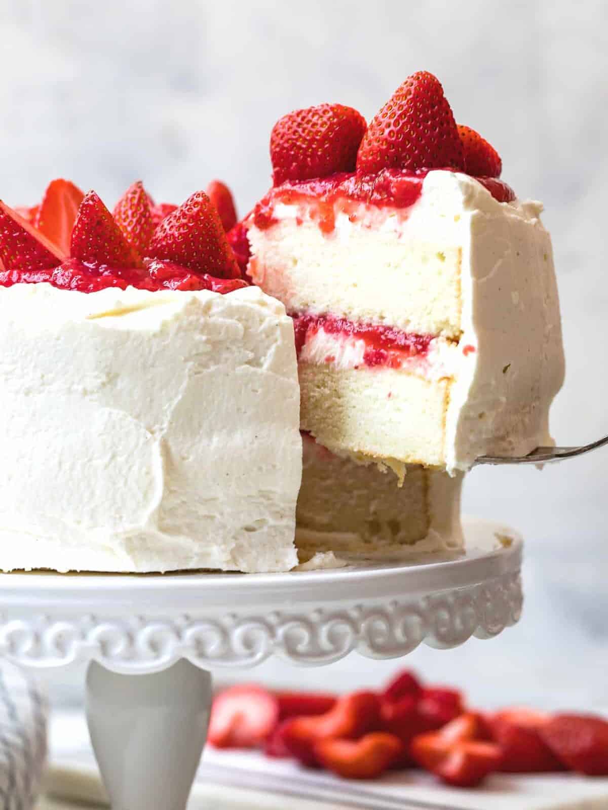 lifting slice of white layer cake with strawberry filling