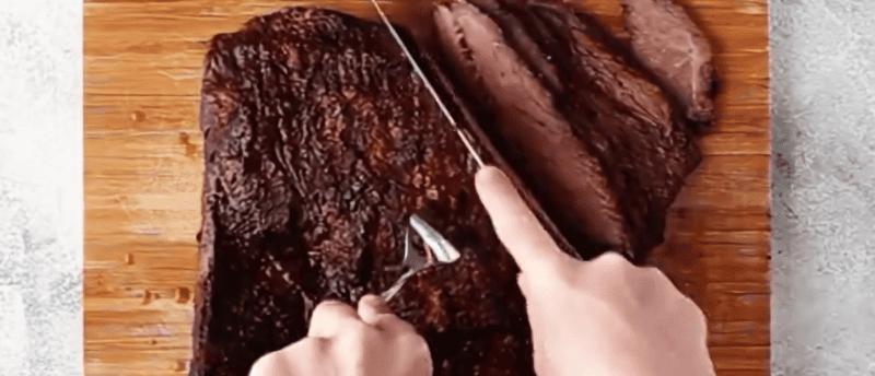 slicing brisket on a wooden cutting board.