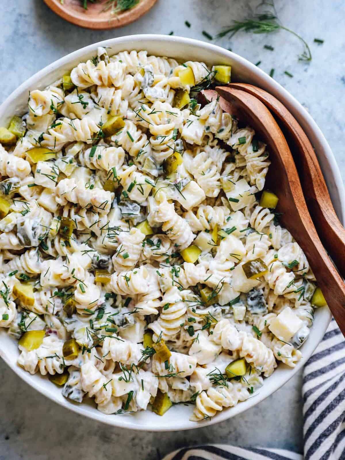 overhead view of dill pickle pasta salad in a white serving bowl with wooden salad tongs.
