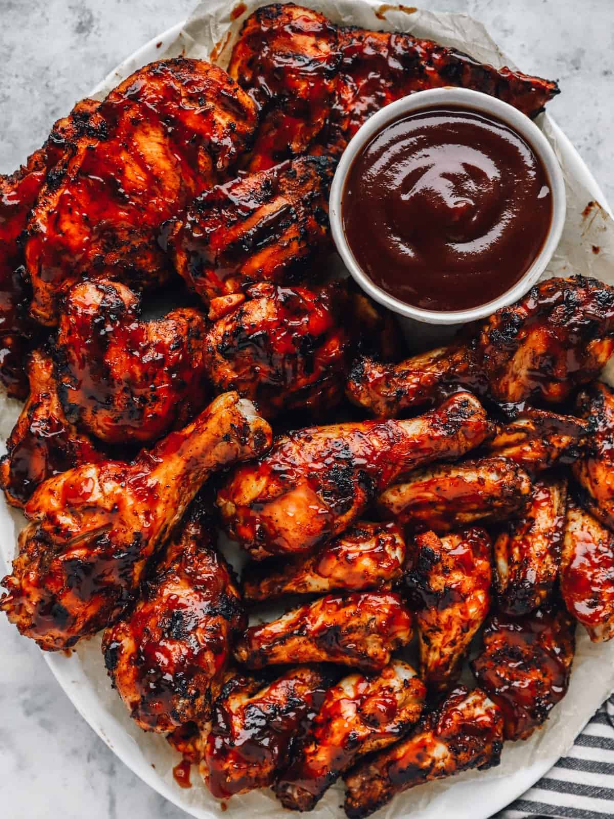 a plate of grilled BBQ chicken pieces, with a small bowl of BBQ sauce