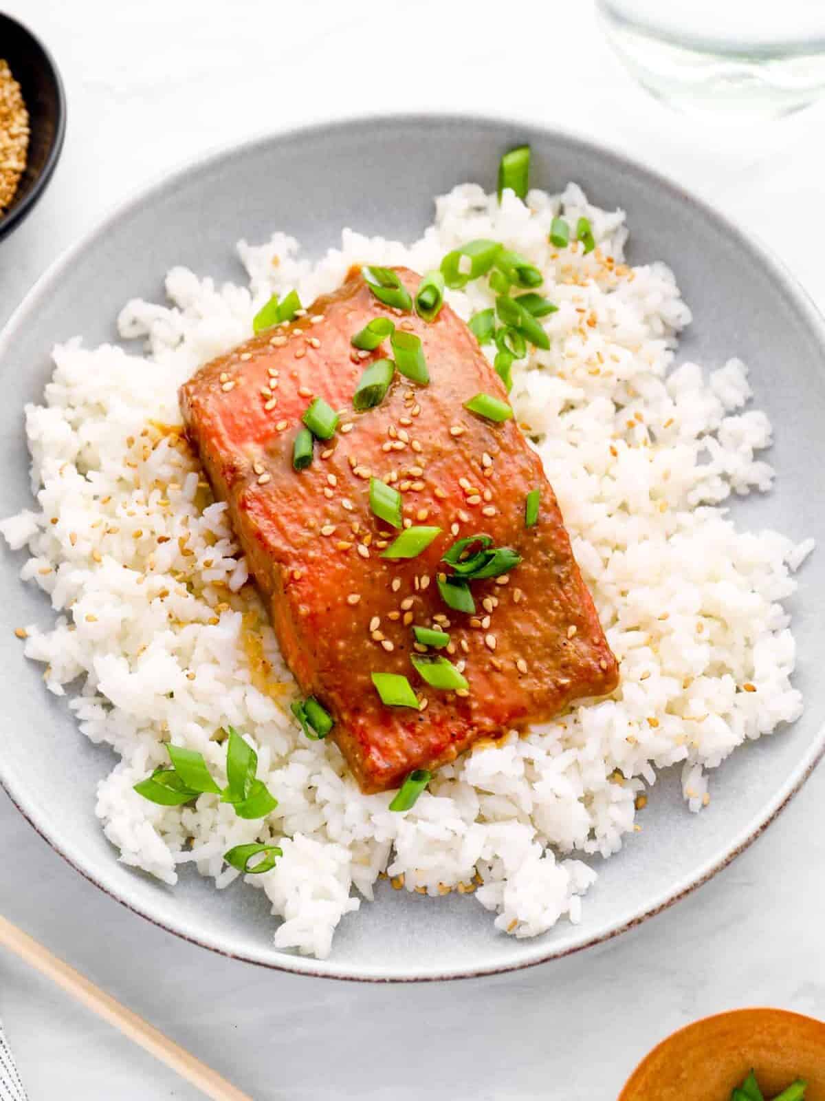 miso glazed salmon on a bed of white rice on a white plate.