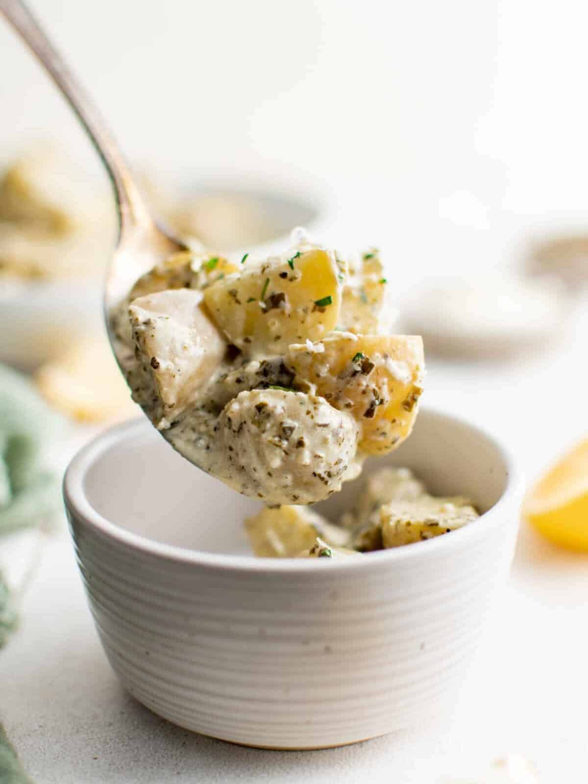 a spoon scooping pesto potato salad from a small white bowl.