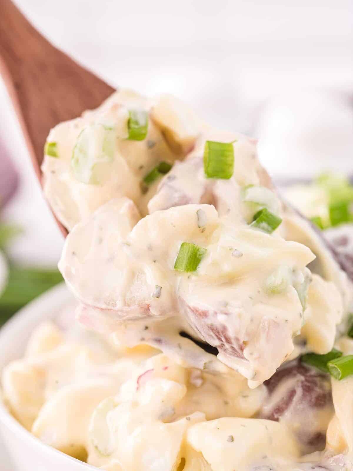 a wooden spoon scooping a spoonful of loaded ranch potato salad from a white bowl.