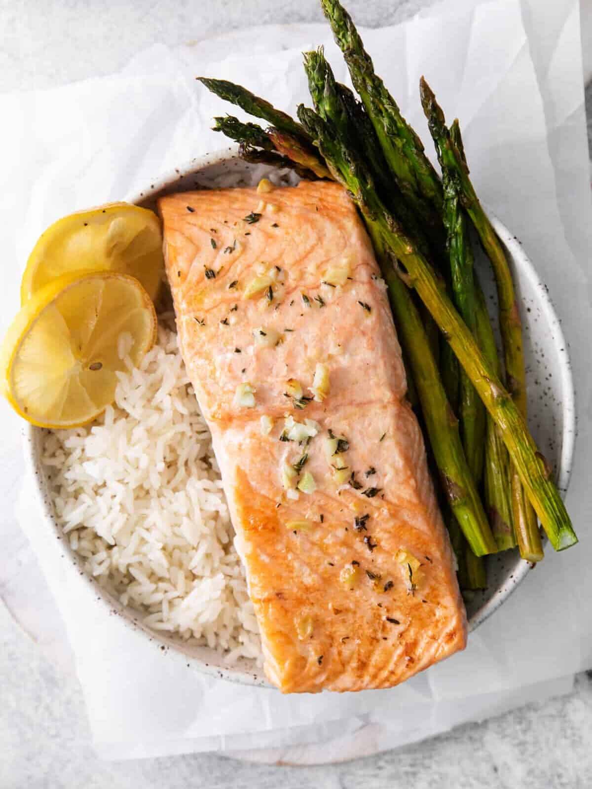 sheet pan lemon salmon on a bed of rice with asparagus in a white bowl.
