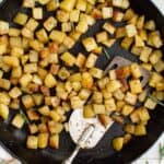 overhead view of breakfast potatoes in a cast iron skillet with a spatula.