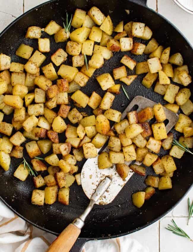 overhead view of breakfast potatoes in a cast iron skillet with a spatula.