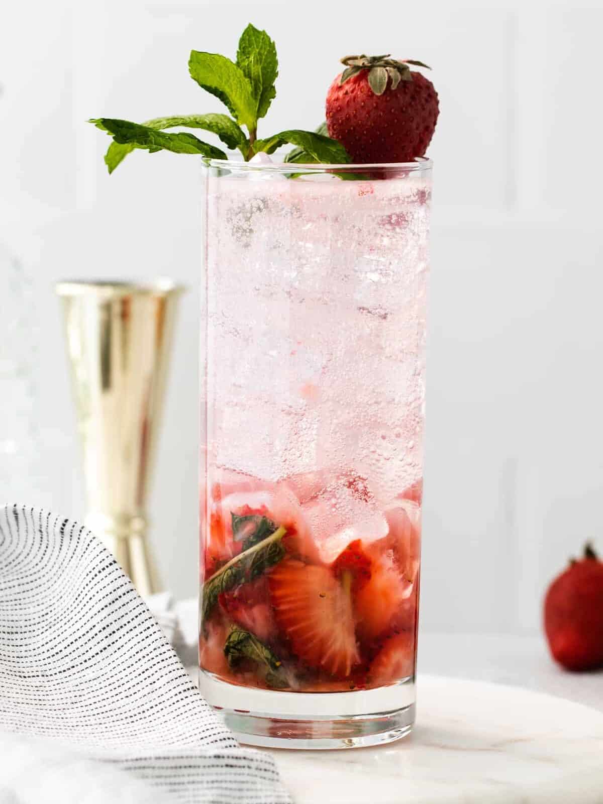 side view of a strawberry mojito in a highball glass topped with mint sprigs and a strawberry.