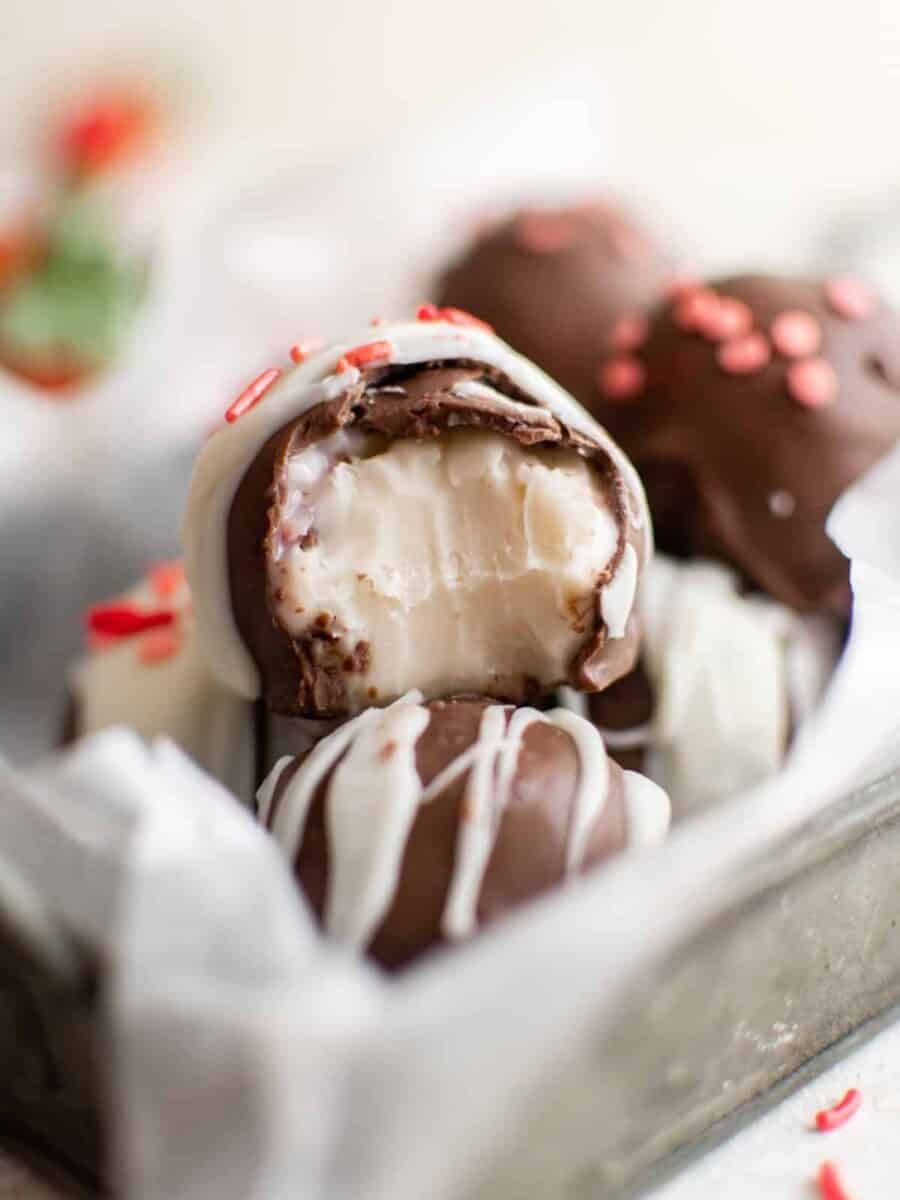 a bitten strawberry truffle on a pile of strawberry truffles in a small parchment lined basket.