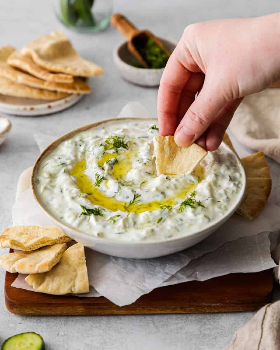 three-quarters view of a hand dipping a pita chip into tzatziki dip.