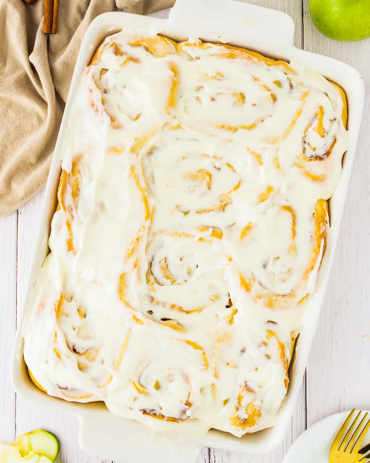 apple pie cinnamon rolls in a white dish with cinnamon sticks.