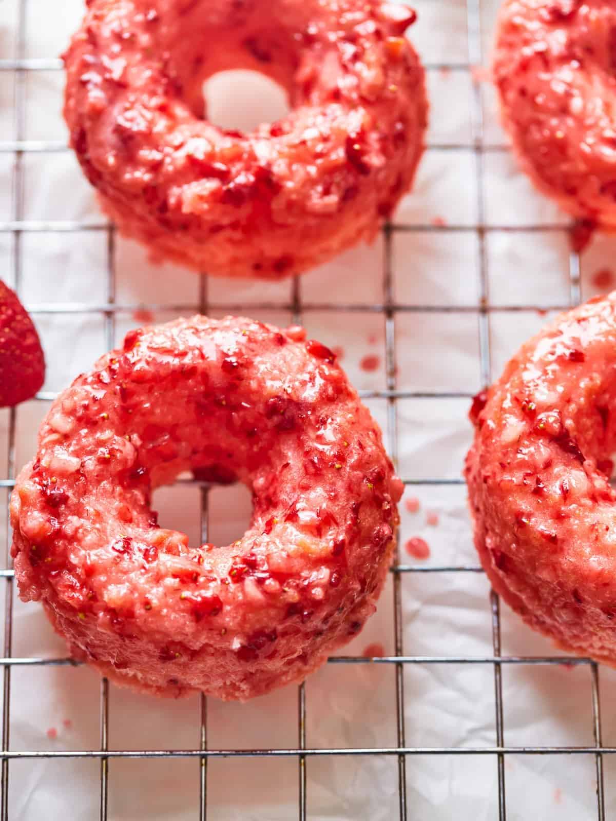 three-quarters view of strawberry donuts on a wire cooling rack.