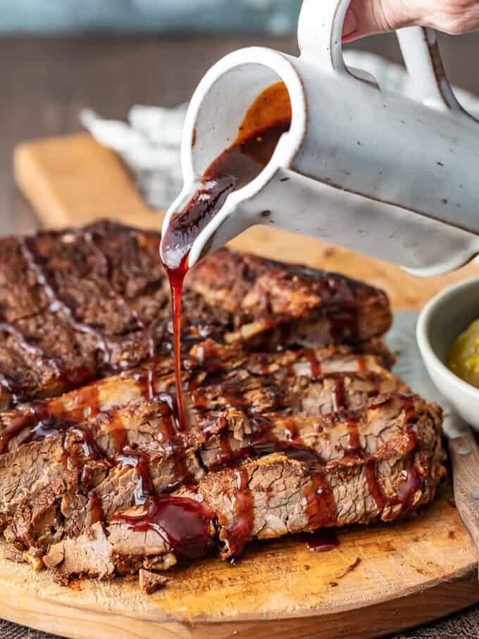 hand pouring barbecue sauce over beef brisket