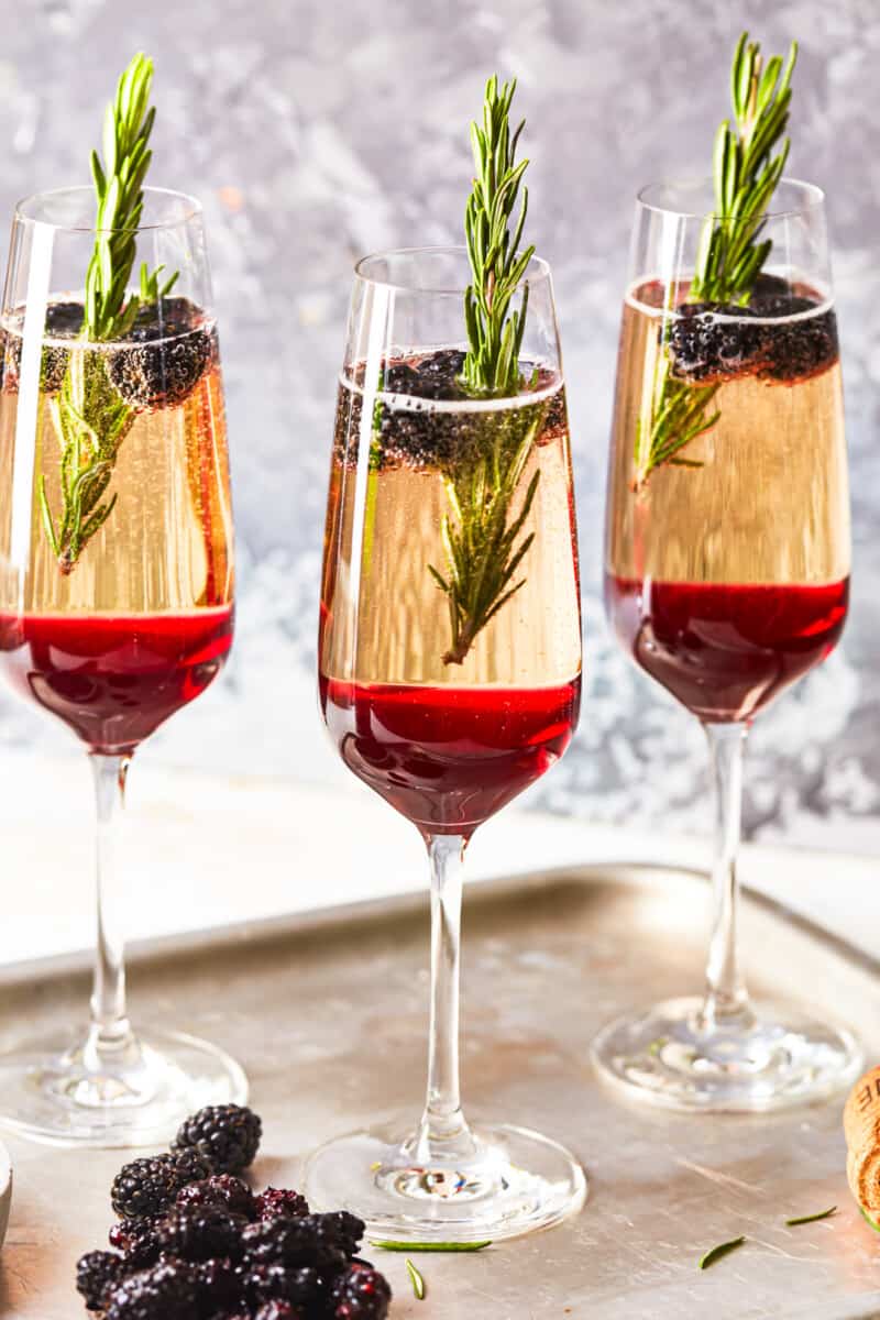 side view of 3 blackberry champagne cocktails on a metal tray.