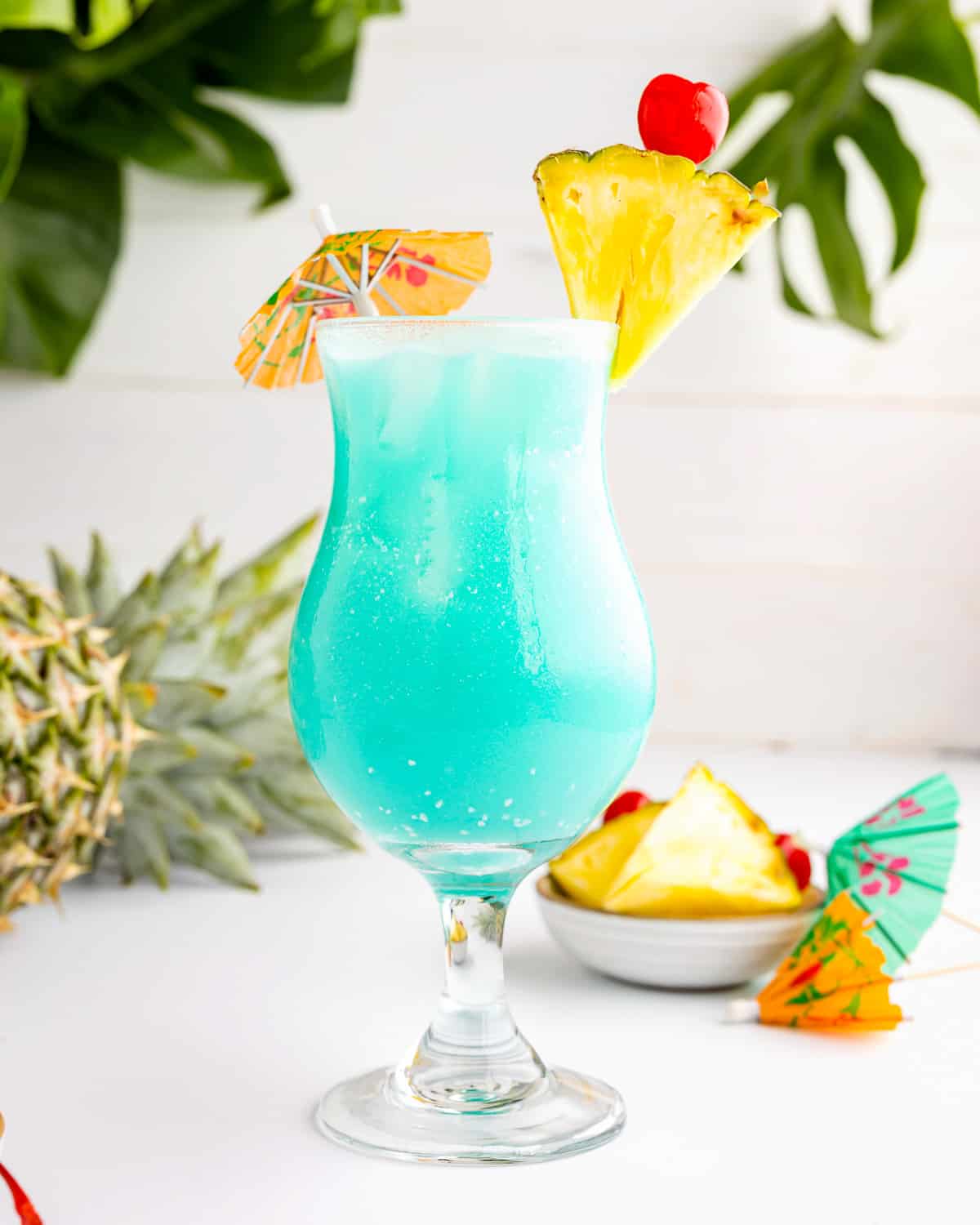 blue hawaiian cocktail with pineapples and decorative umbrellas.