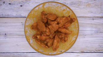 chicken wings tossed in buffalo sauce in a glass bowl.