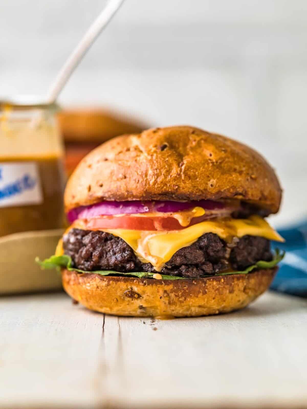 front view of a cheeseburger, with a jar of sauce off to the side