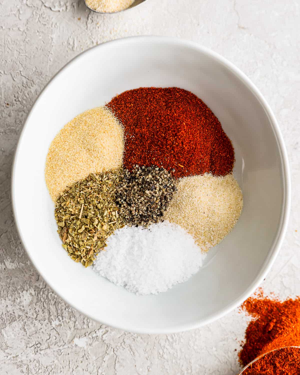 a colorful array of herbs and spices in a white bowl, before being mixed together to create burger seasoning.