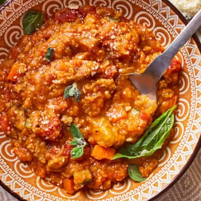 overhead view of a serving of sausage lentil soup in a patterned bowl with a spoon.