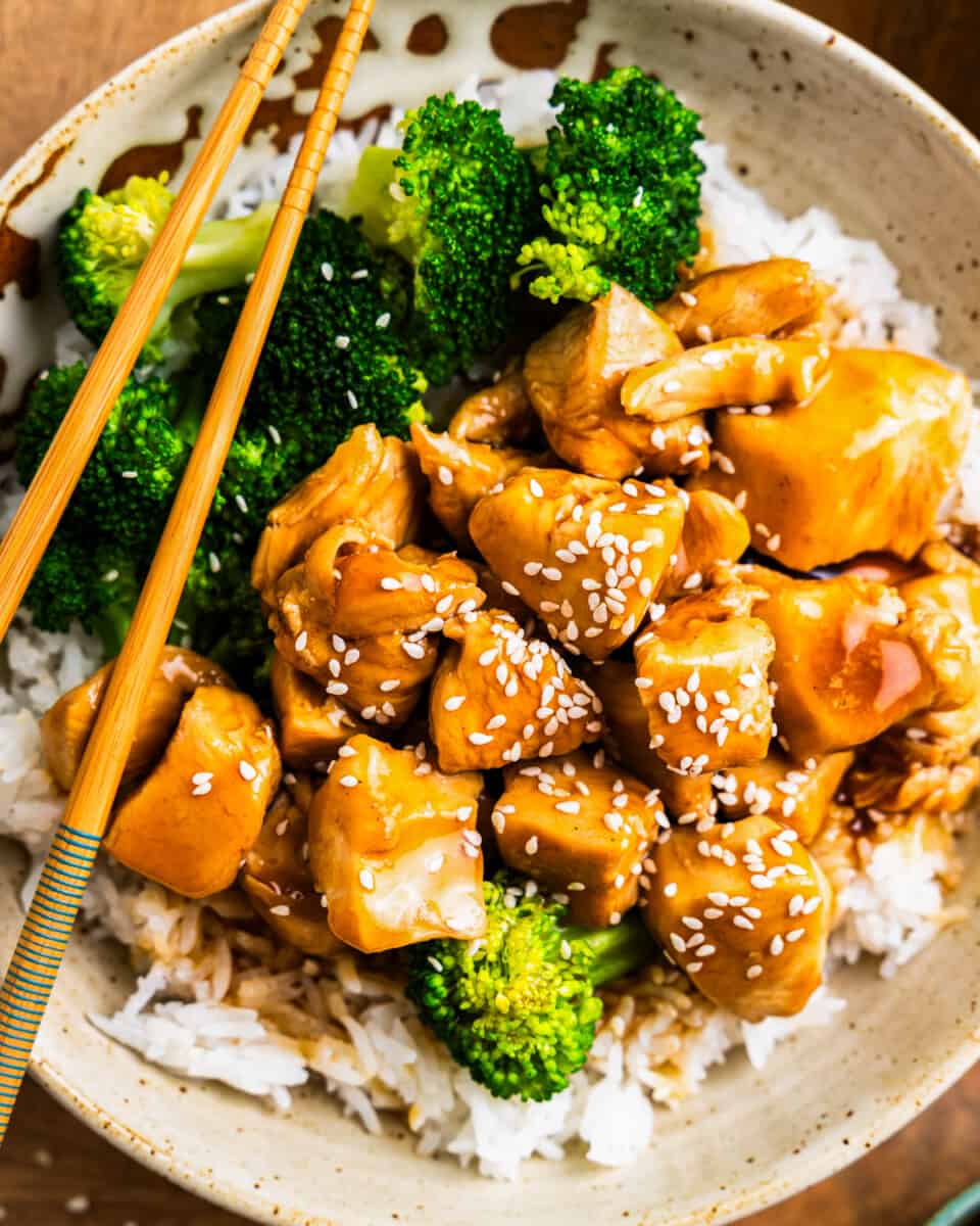 close up overhead view of teriyaki chicken in a white bowl with rice and broccoli and chopsticks.